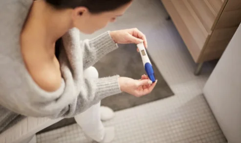 Woman sitting on the bathroom floor looking at a pregnancy test